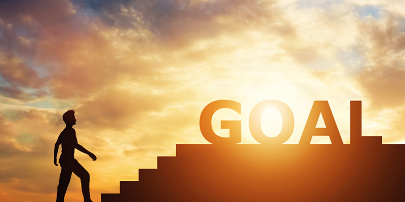 Man standing in front of stairs with "goal" writing on top. Career and achievement pursuit. Aspirations.